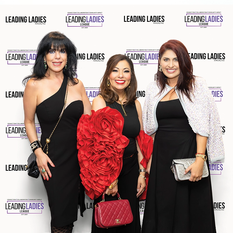 Three women smiling in front of logo wall.