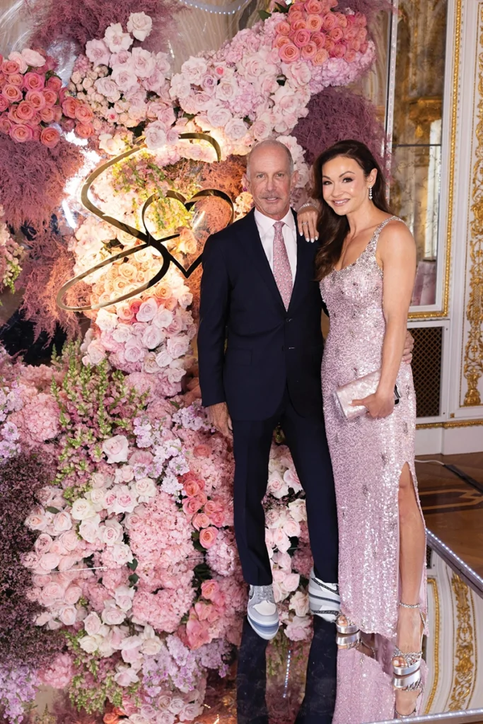 A man and a woman smiling, with flower arrangement in background.