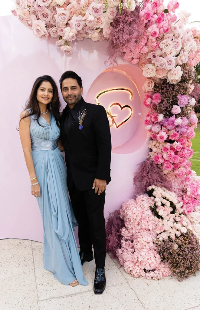A man and a woman smiling with flower arrangement in background.