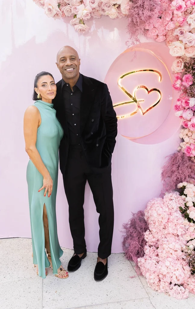 A man and a woman smiling with flower arrangement in the background.