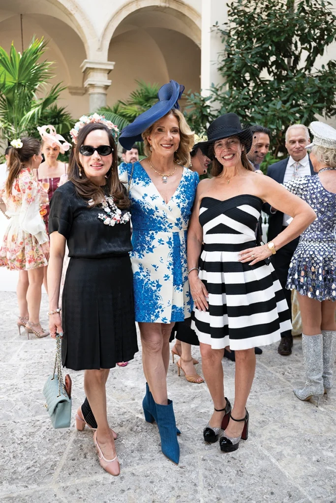 Three women smiling, wearing dress hats.