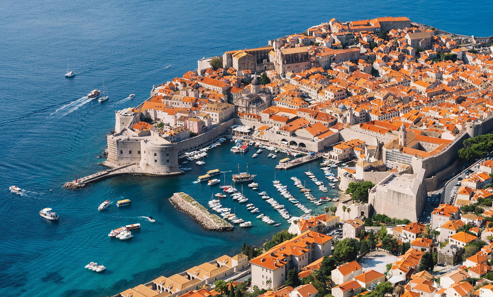 An aerial view of city surrounded by ocean and yachts.