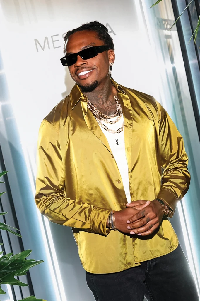 Man with sunglasses and gold chains, smiling.