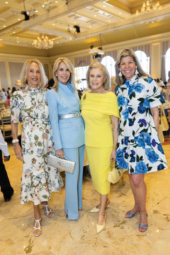 Four women smiling, standing, full body.