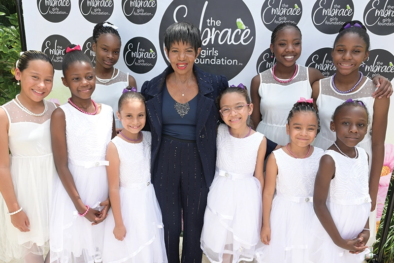 Girls in dresses surrounding a woman in a suit.