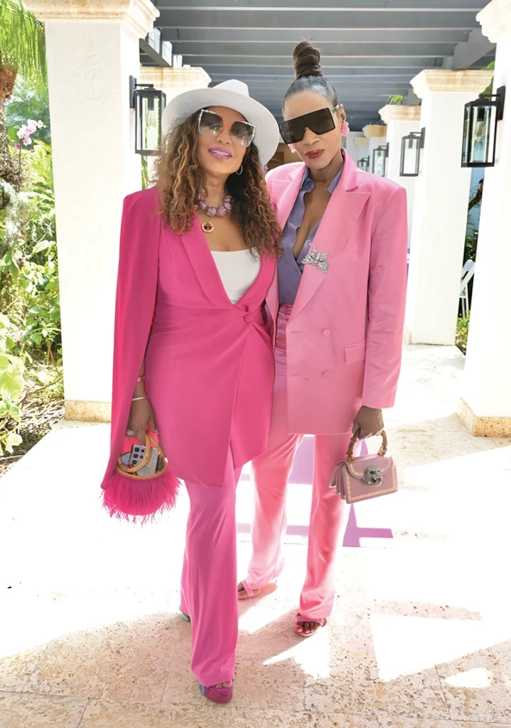 Two women wearing sunglasses, smiling and standing, full body.