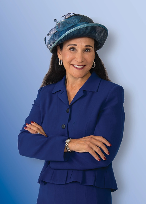 A woman in blue suit smiling, wearing blue dress hat.