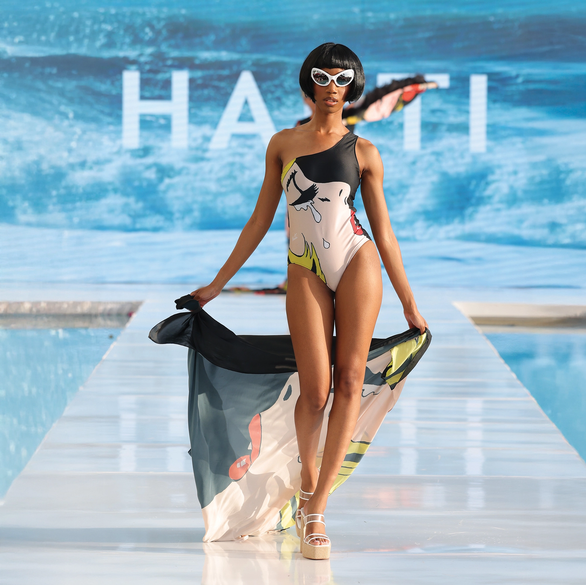 A woman in bathing suit walking on a runway.