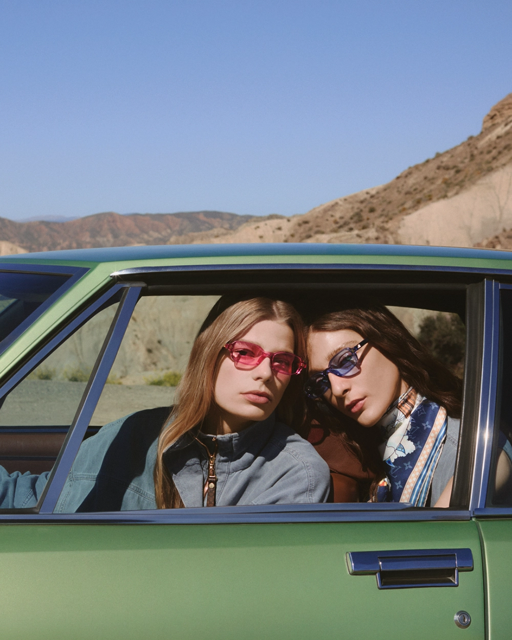 Two women sitting in car, wearing sunglasses.